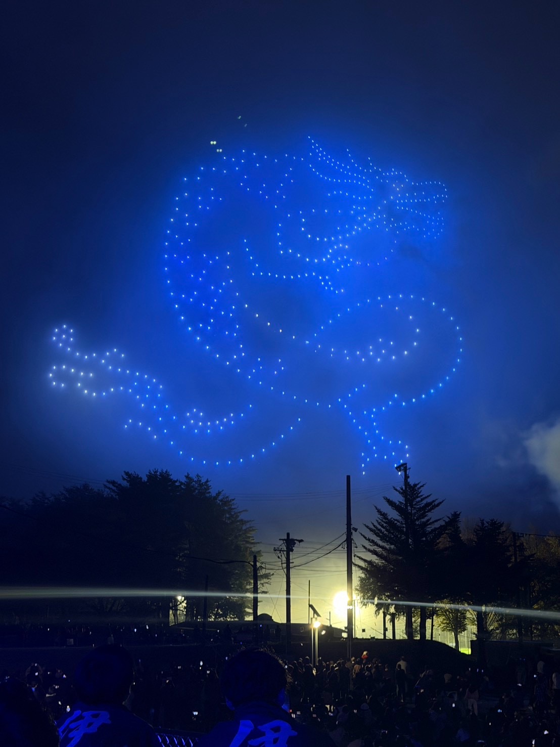 大芝高原の夜空に青い光で描かれたドローンショーを見上げる観客